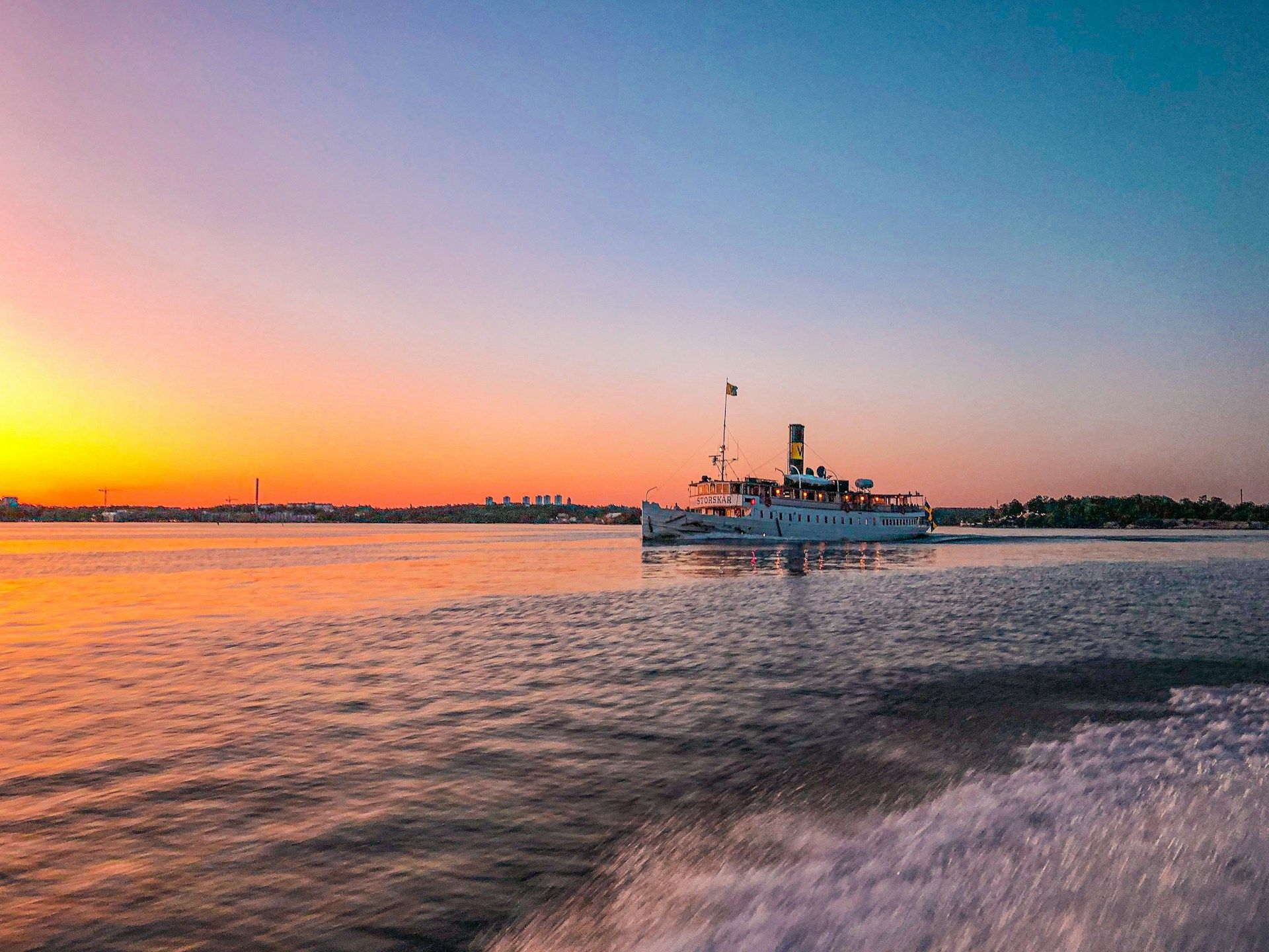 A white ship sails on calm water in the Stockholm archipelago during a vibrant orange sunset.