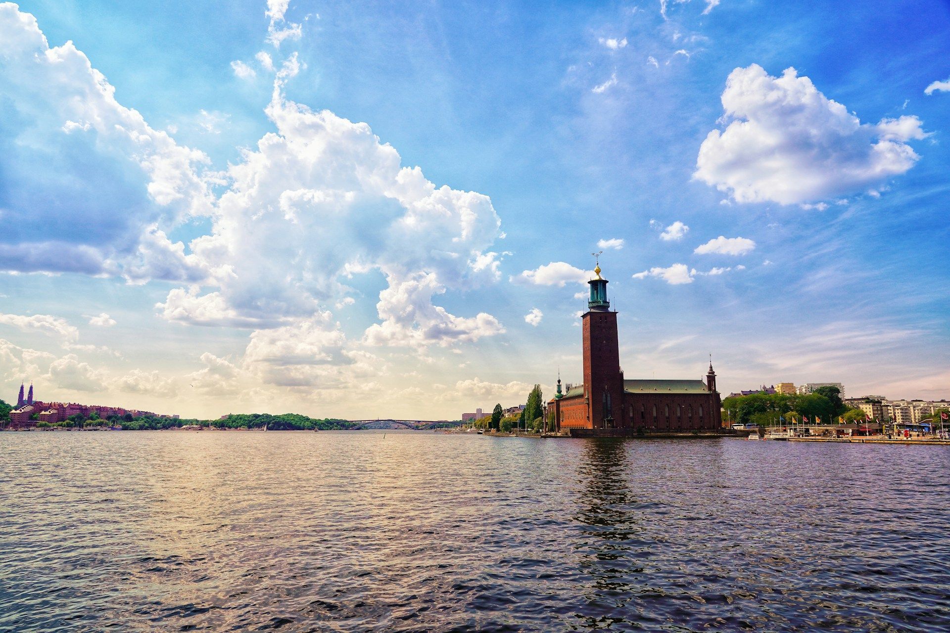 Stockholm City Hall standing on the waterfront under a vibrant blue sky with fluffy white clouds.