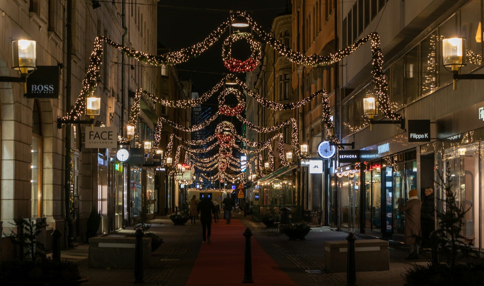 A nighttime view in Stockholm with glowing holiday lights and wreaths hanging overhead.