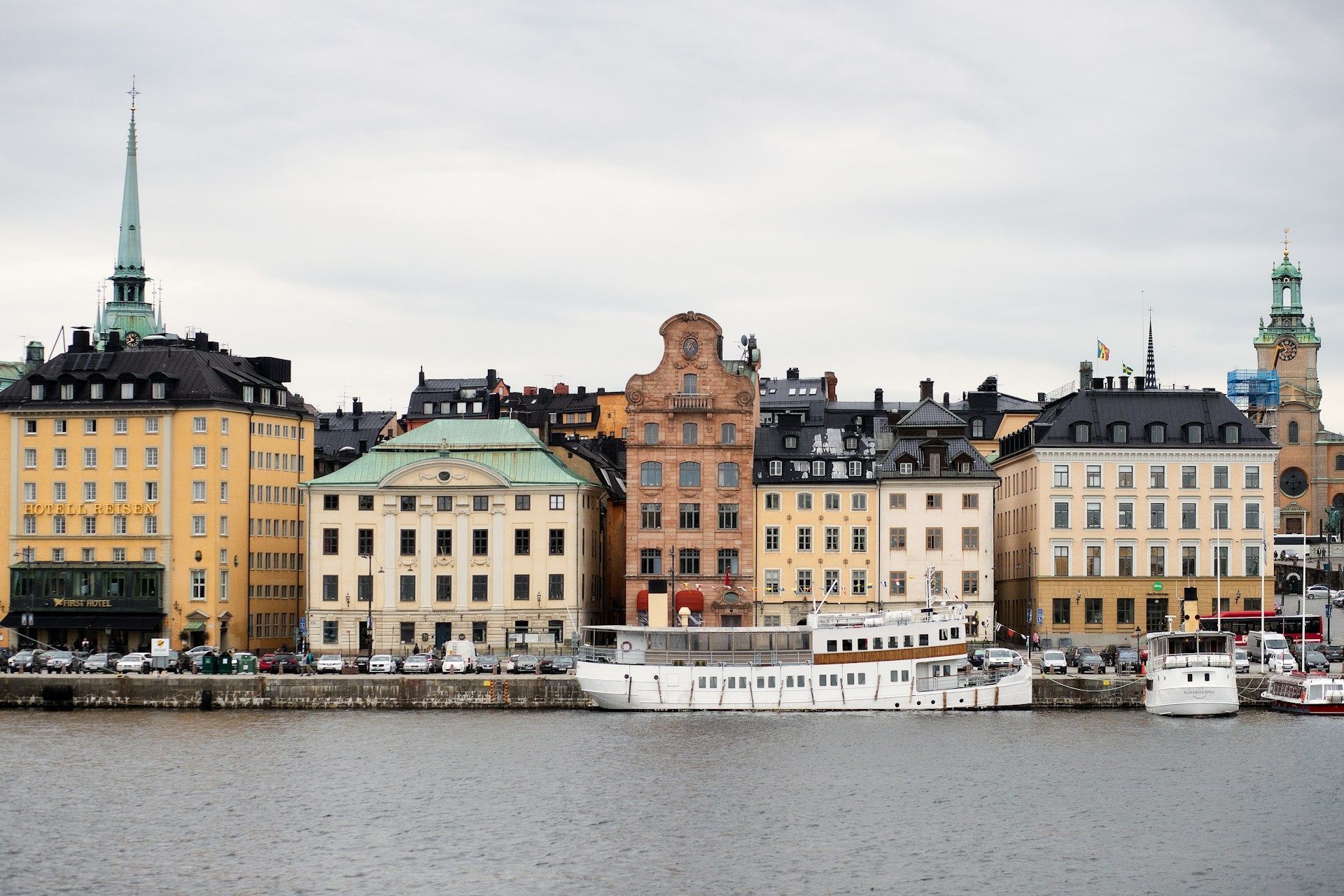 Stockholm waterfront cityscape featuring a row of historic, colorful buildings and a docked white boat under a gray sky.