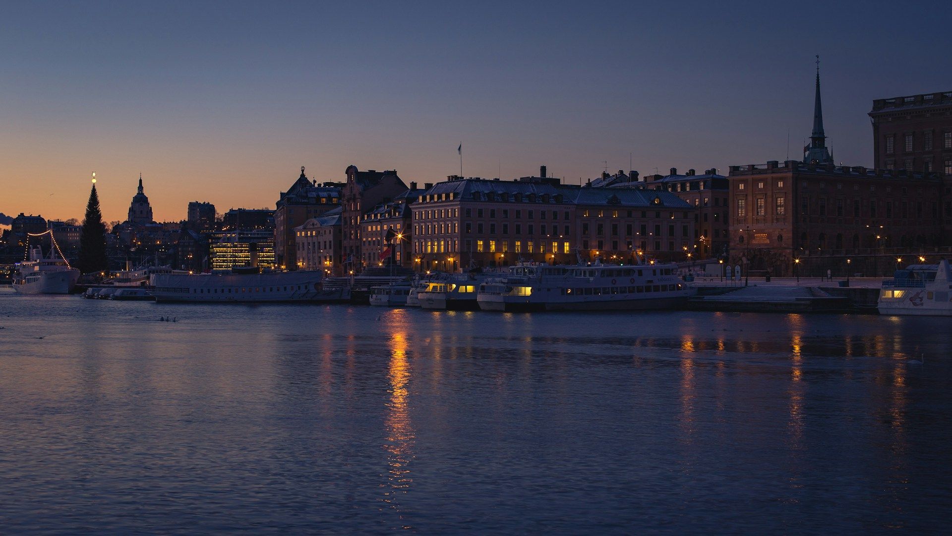 A twilight cityscape of Gamla Stan, Stockholm, Sweden, featuring illuminated buildings and boats.