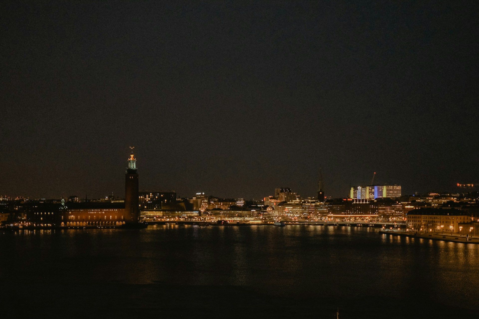 Nighttime view of Stockholm's city skyline and City Hall illuminated against a dark sky, reflected in the water.