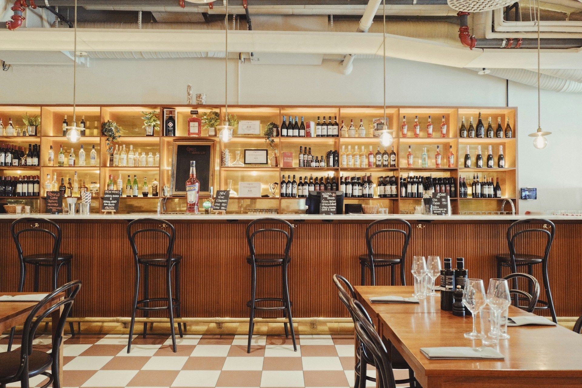 An empty restaurant bar with wooden stools, a checkered floor, and shelves in Stockholm.