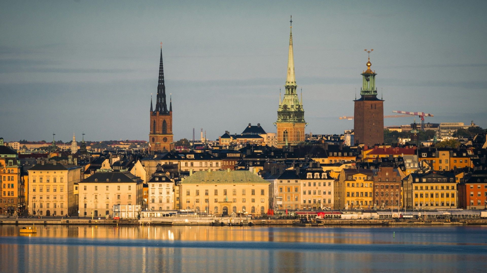 Stockholm skyline featuring church spires and historic buildings reflecting over the water at sunset.