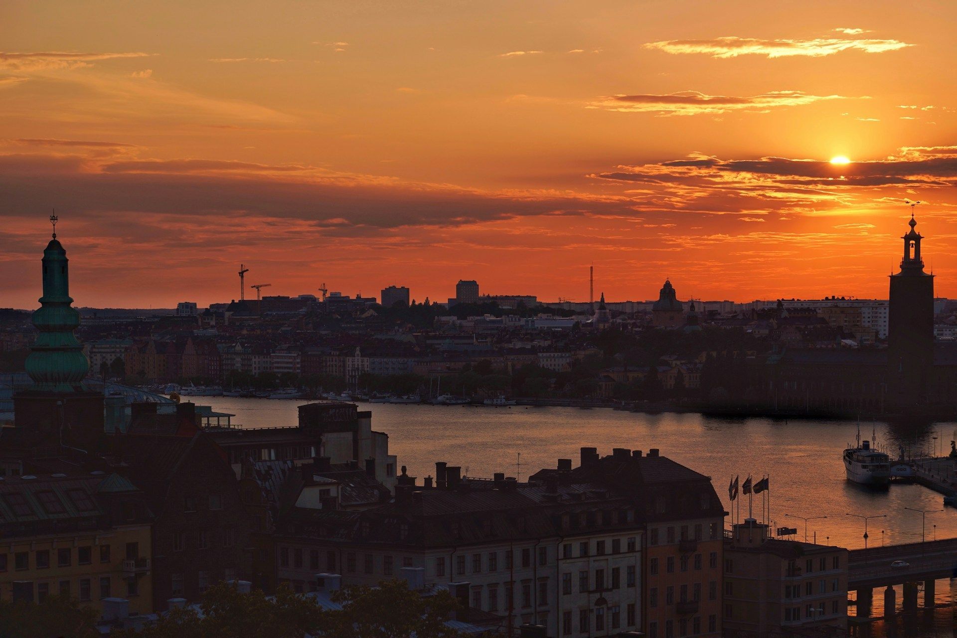 Stockholm cityscape at sunset with silhouettes of city hall and historic buildings overlooking the water.