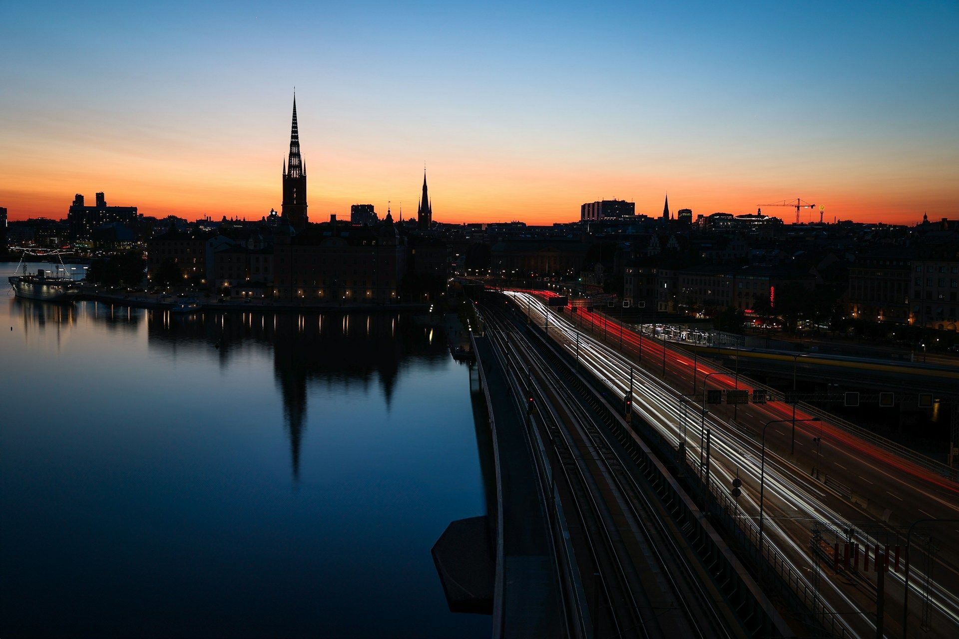 Stockholm skyline at dusk, featuring Riddarholmen Church's silhouette, reflected in calm water.