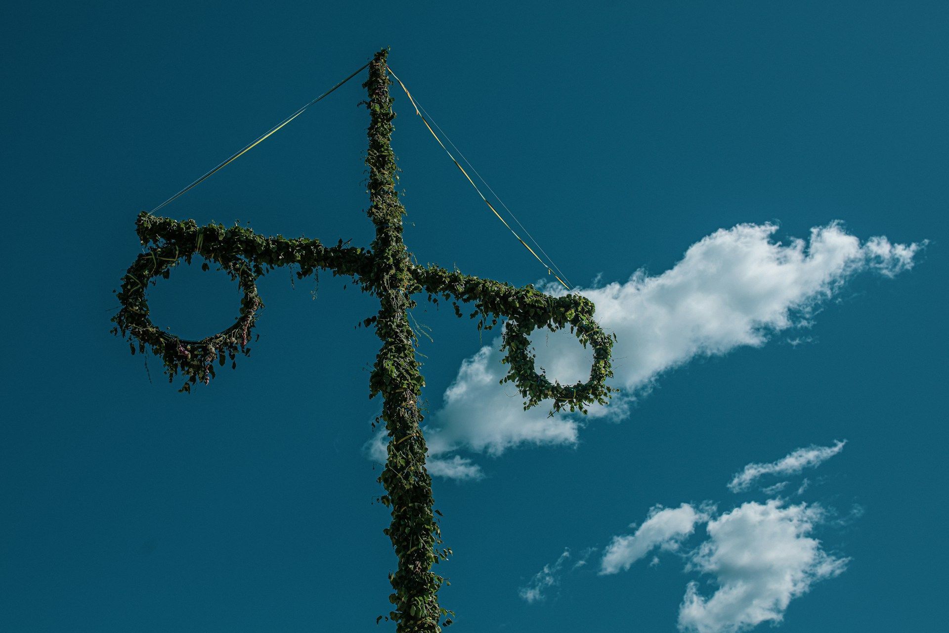 A traditional Swedish Midsummer pole decorated with green leaves and two wreaths.