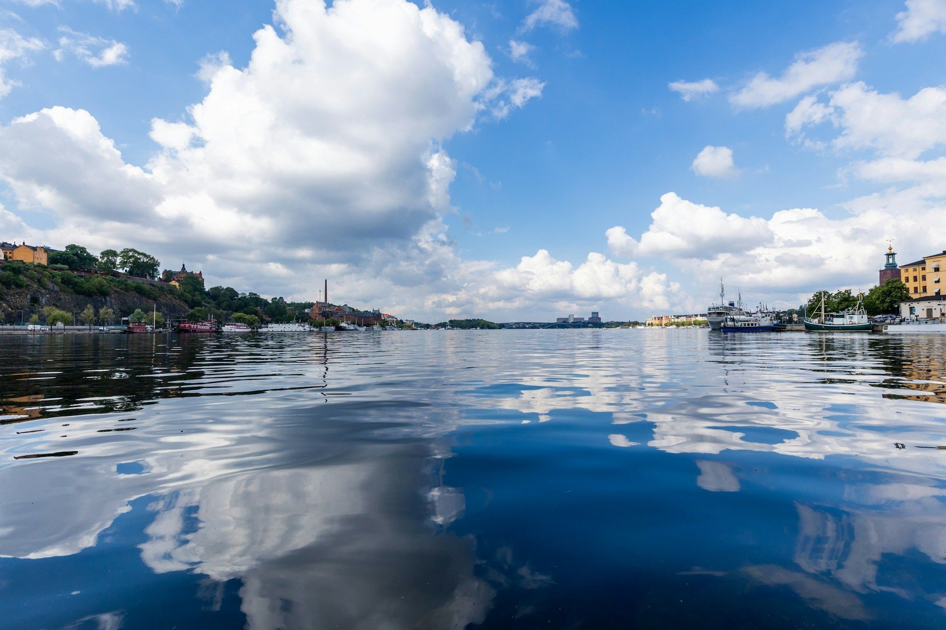 Watery expanse in Stockholm with sky reflected, buildings on shores, fluffy clouds.