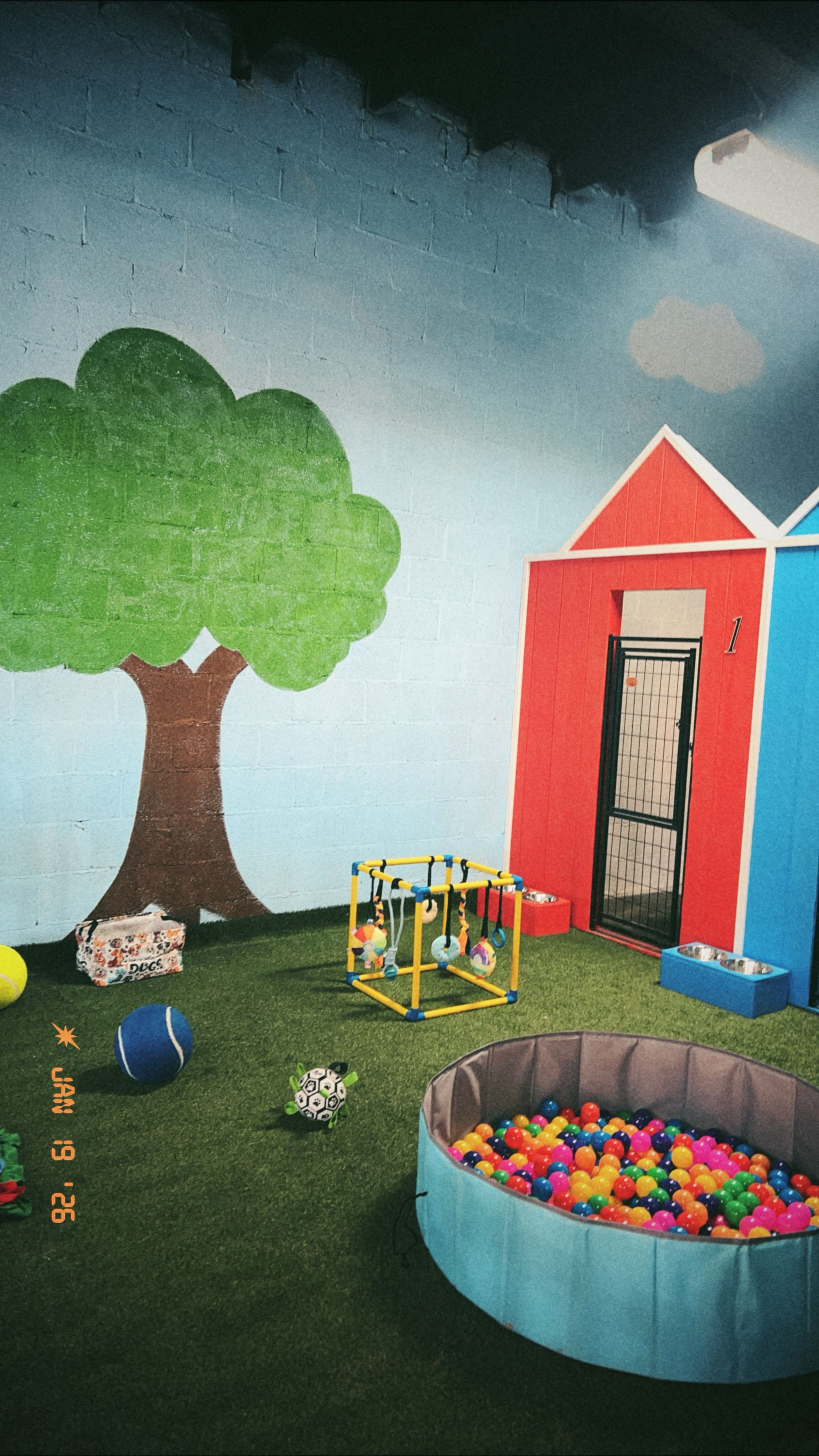 Playroom scene with a tree, houses, and ball pit. Blue, red, green, and brown colors.
