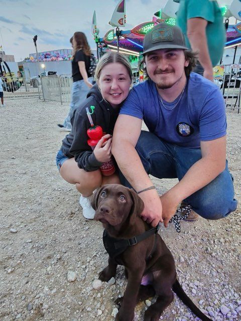A young couple with a brown puppy at a fair, smiling.