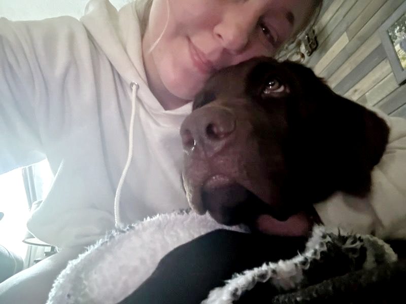 Woman in white hoodie cuddling a brown dog; both smiling.