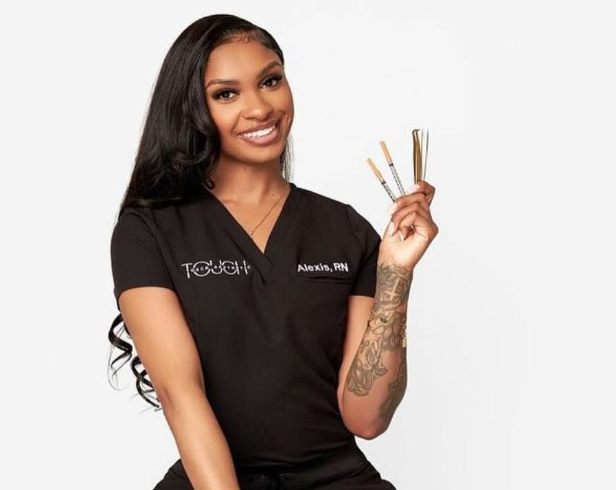A woman in a black scrub top is holding three pens in her hand.