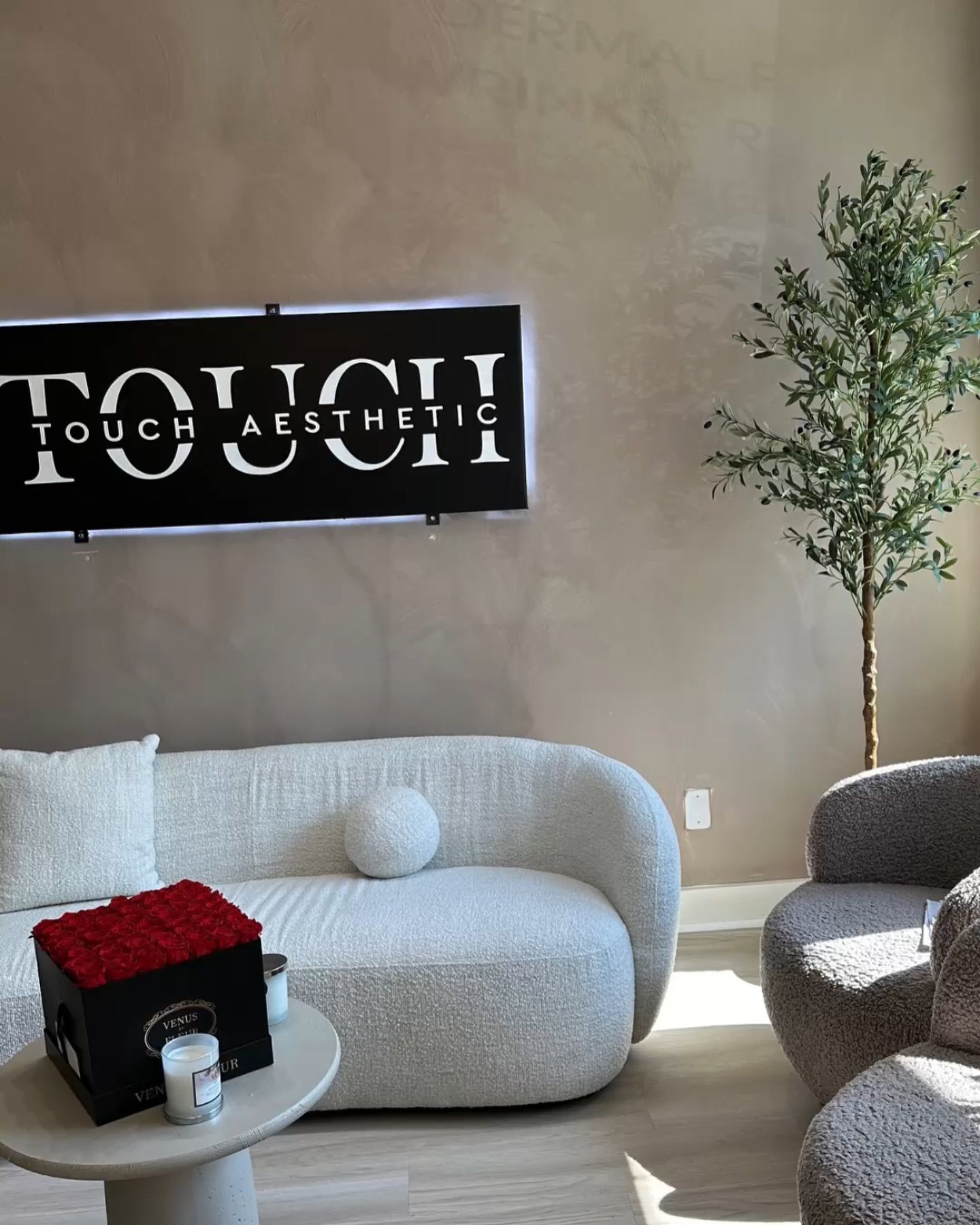 A woman in scrubs is sitting on a couch in front of a sign.