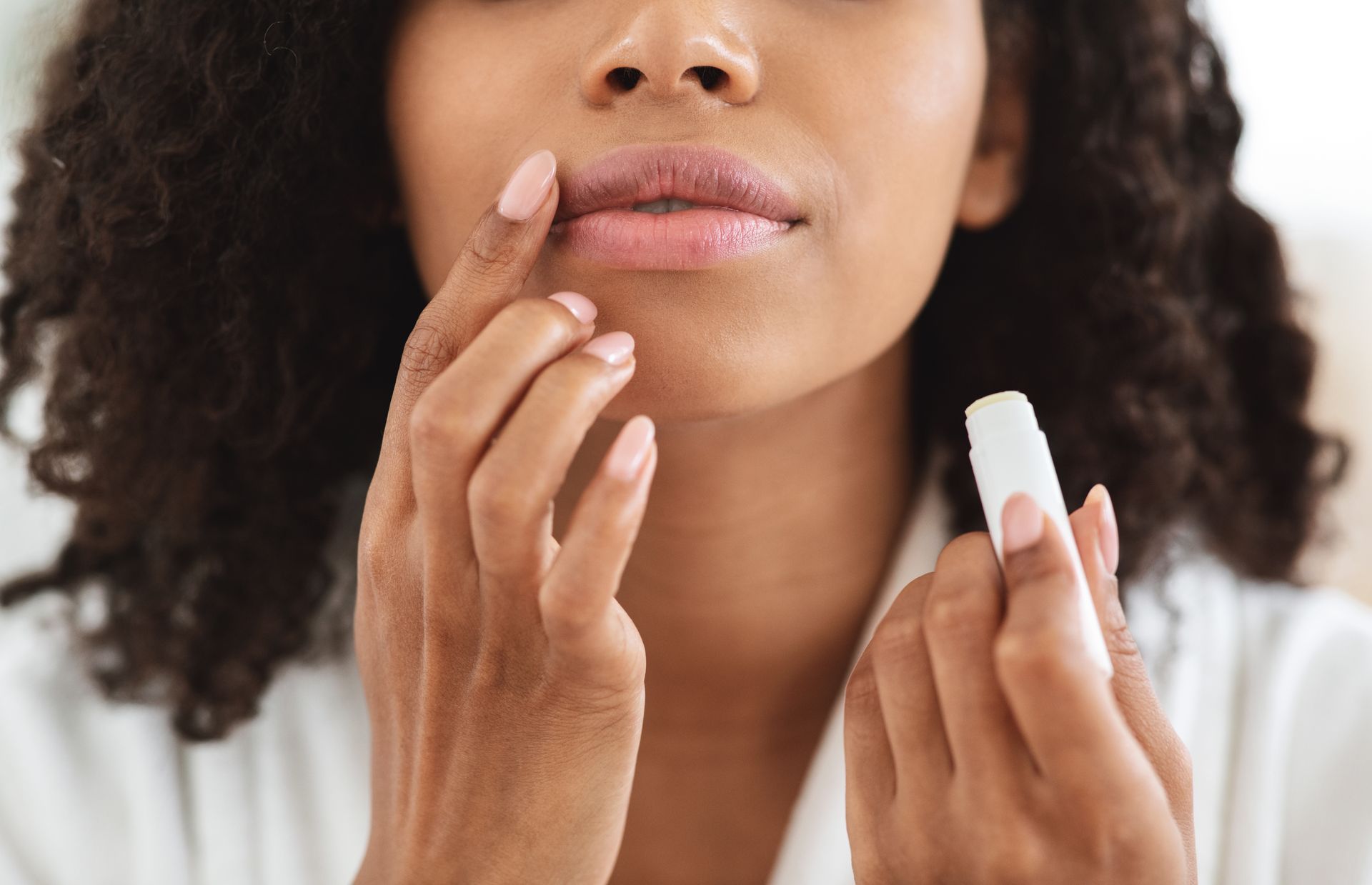 A woman is applying lip balm to her lips.