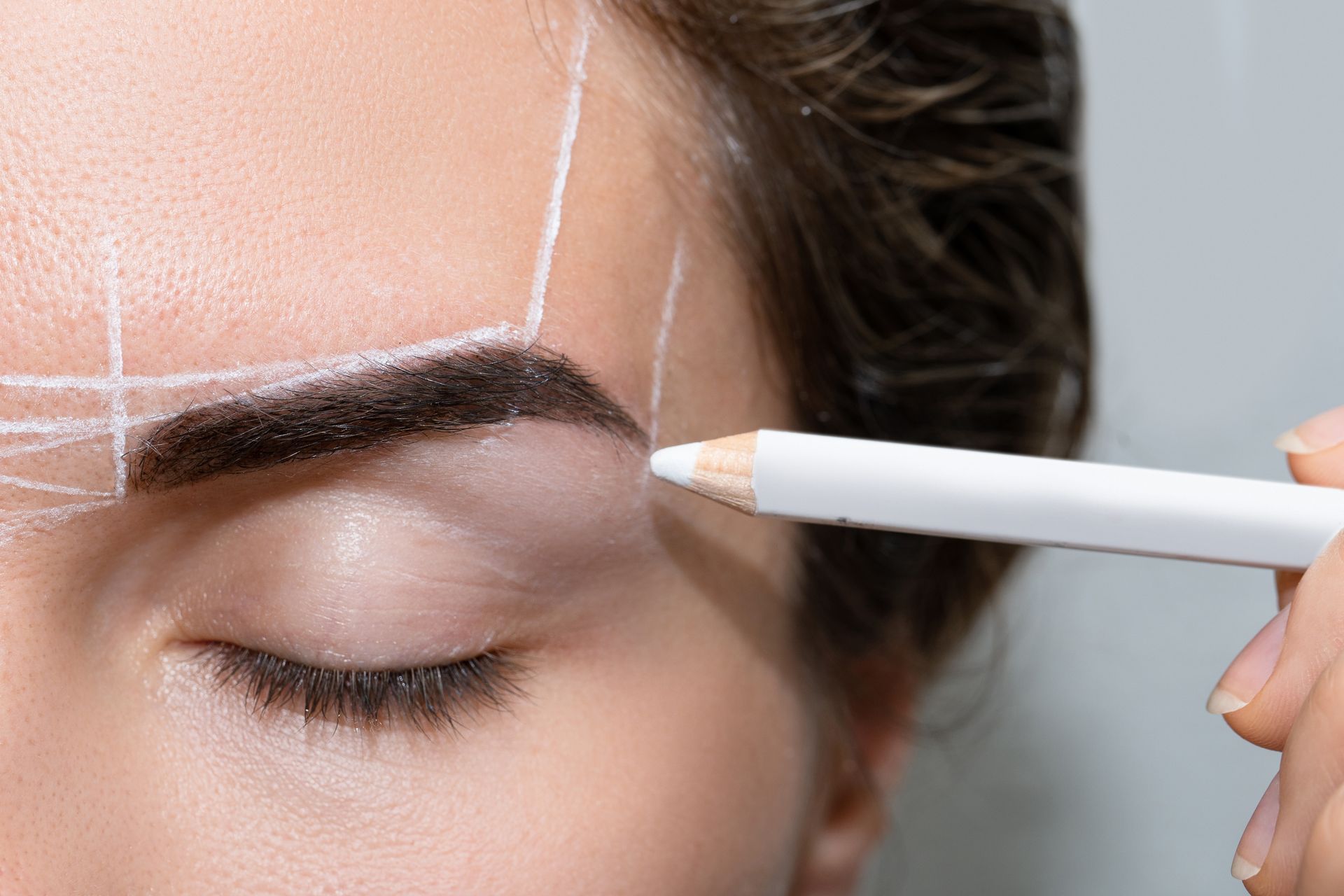 A woman is getting her eyebrows drawn with a pencil.