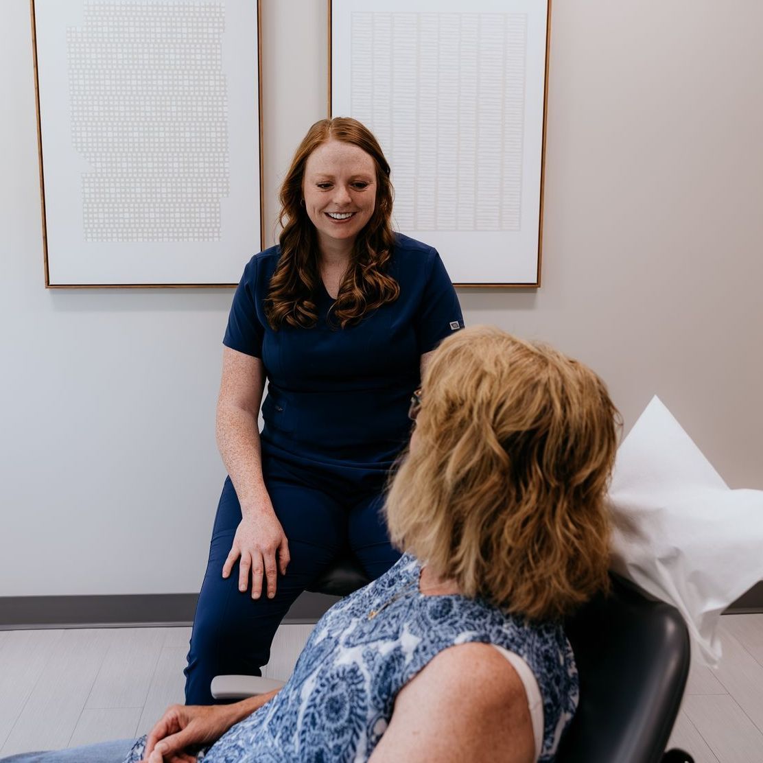 A woman wearing glasses and a blue sweater is sitting on a yellow couch.