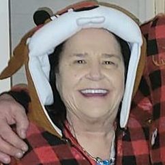 A woman wearing a dog hat and a plaid shirt is smiling.