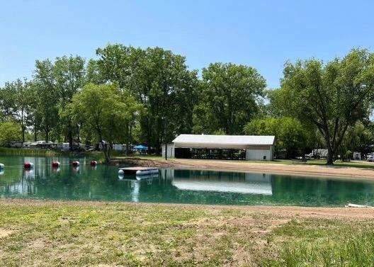 A large body of water surrounded by trees and grass with a white building in the background.