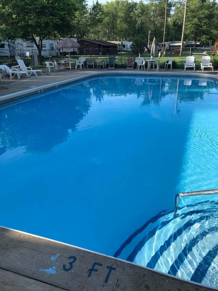 A large swimming pool is surrounded by chairs and trees.