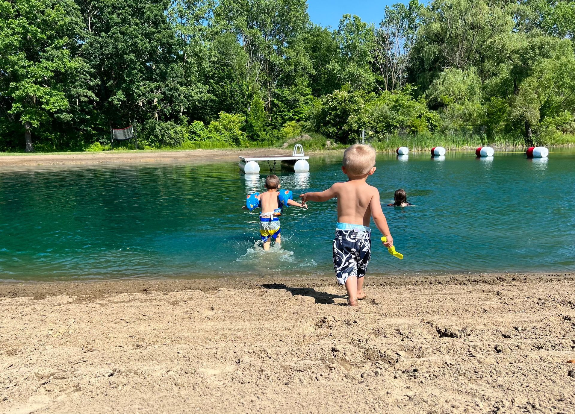 A little boy is standing on a sandy beach next to a lake.