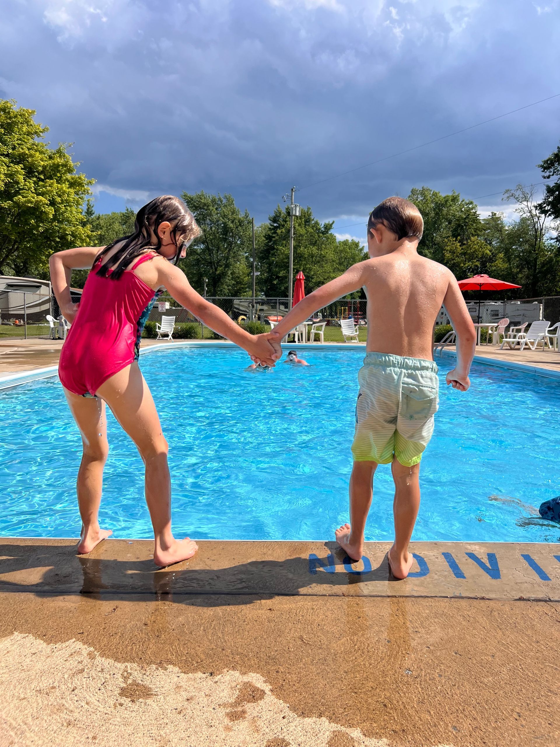 A boy and a girl are holding hands in front of a swimming pool.