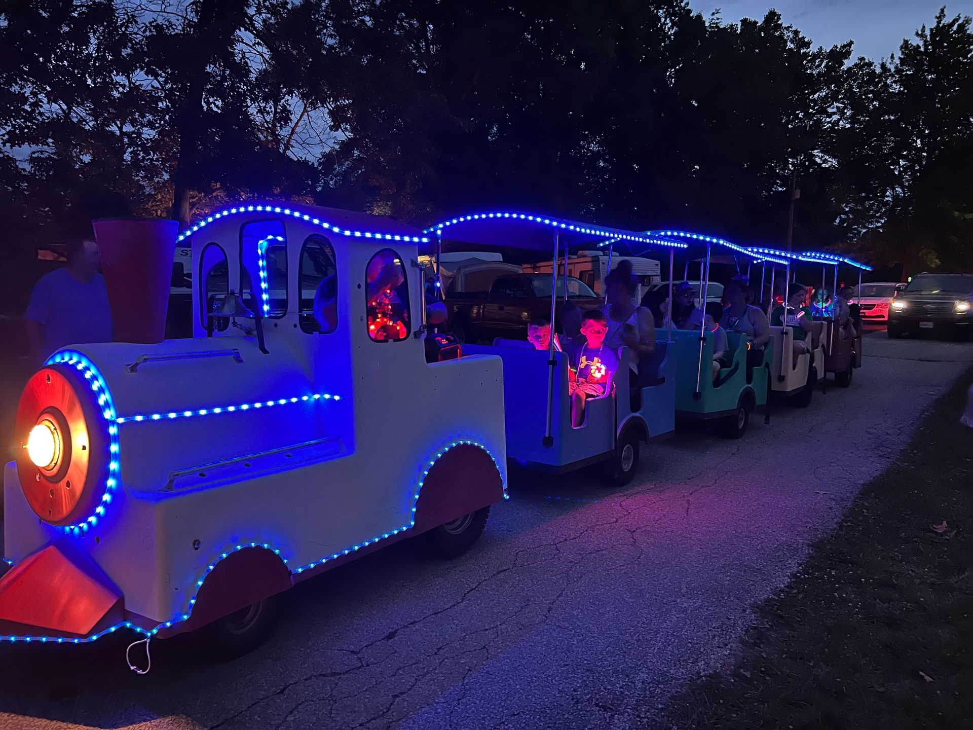 A train is lit up with blue lights and is going down the road.