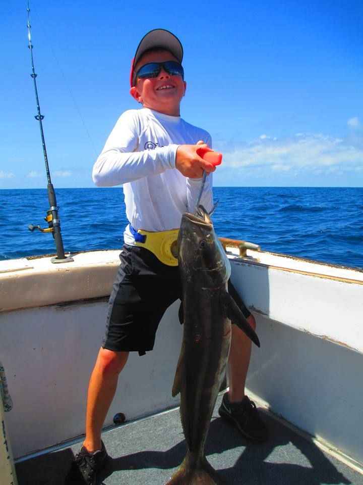 A young boy is holding a large fish on a boat