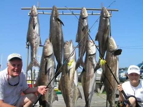 A man and a boy are holding fishing rods in front of a rack of fish