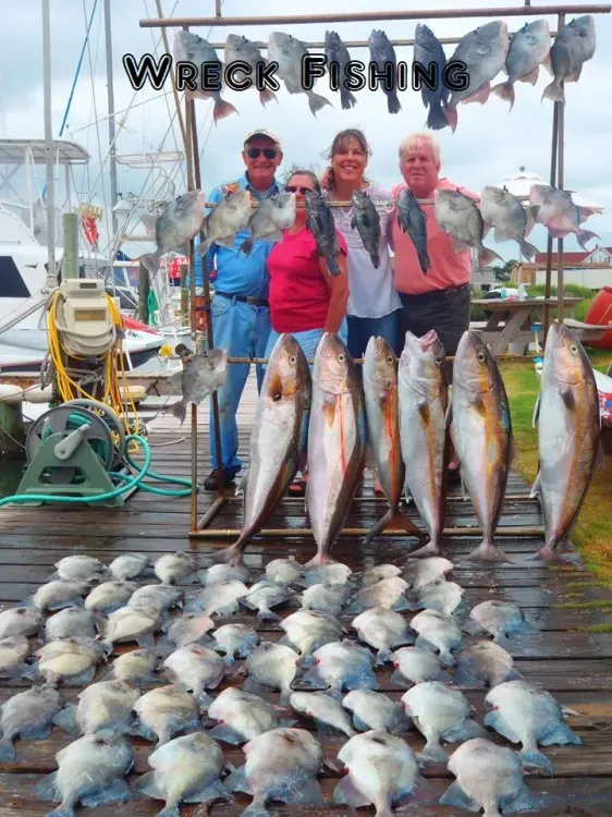 A group of people are posing for a picture with lots of fish on a dock.