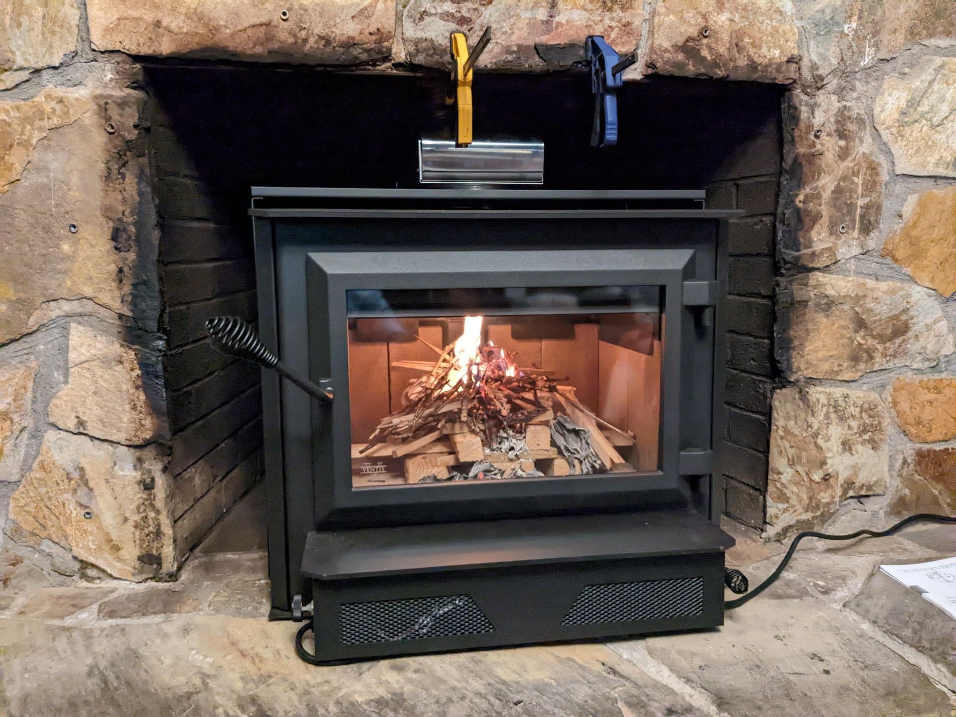 a wood stove is sitting in the corner of a stone fireplace .