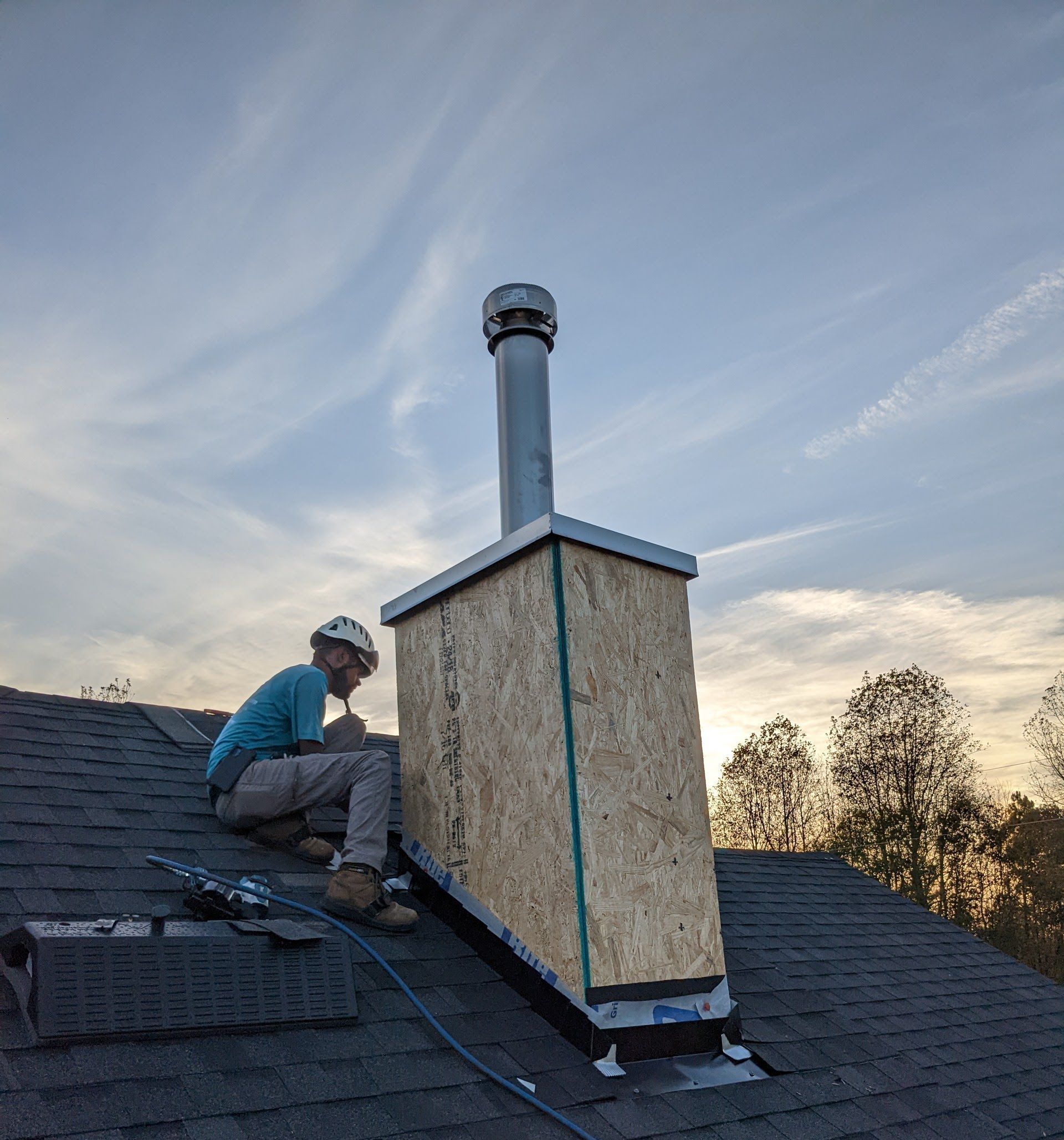 a man is sitting on top of a roof next to a chimney .