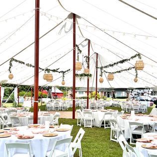 A large tent with tables and chairs set up for a wedding reception.