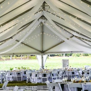 A tent with tables and chairs set up for a wedding reception.