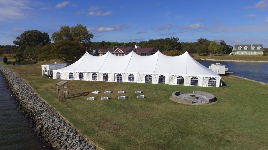 A large white tent is sitting on top of a lush green field next to a body of water.
