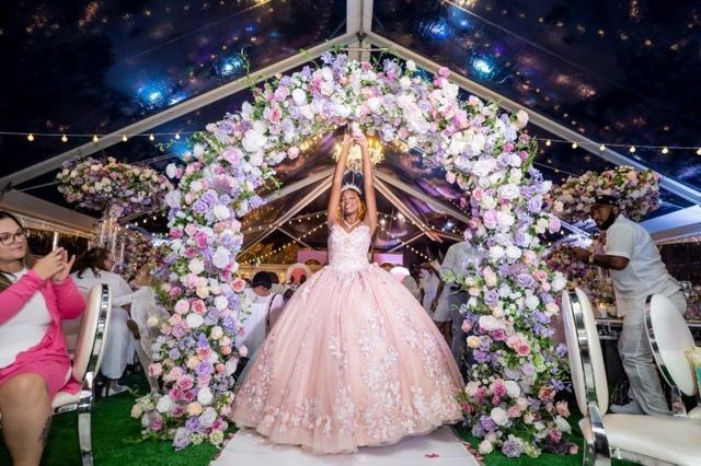 A woman in a pink dress is standing under a tent with flowers.