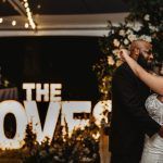 A bride and groom are dancing in front of a sign that says `` the love ''.