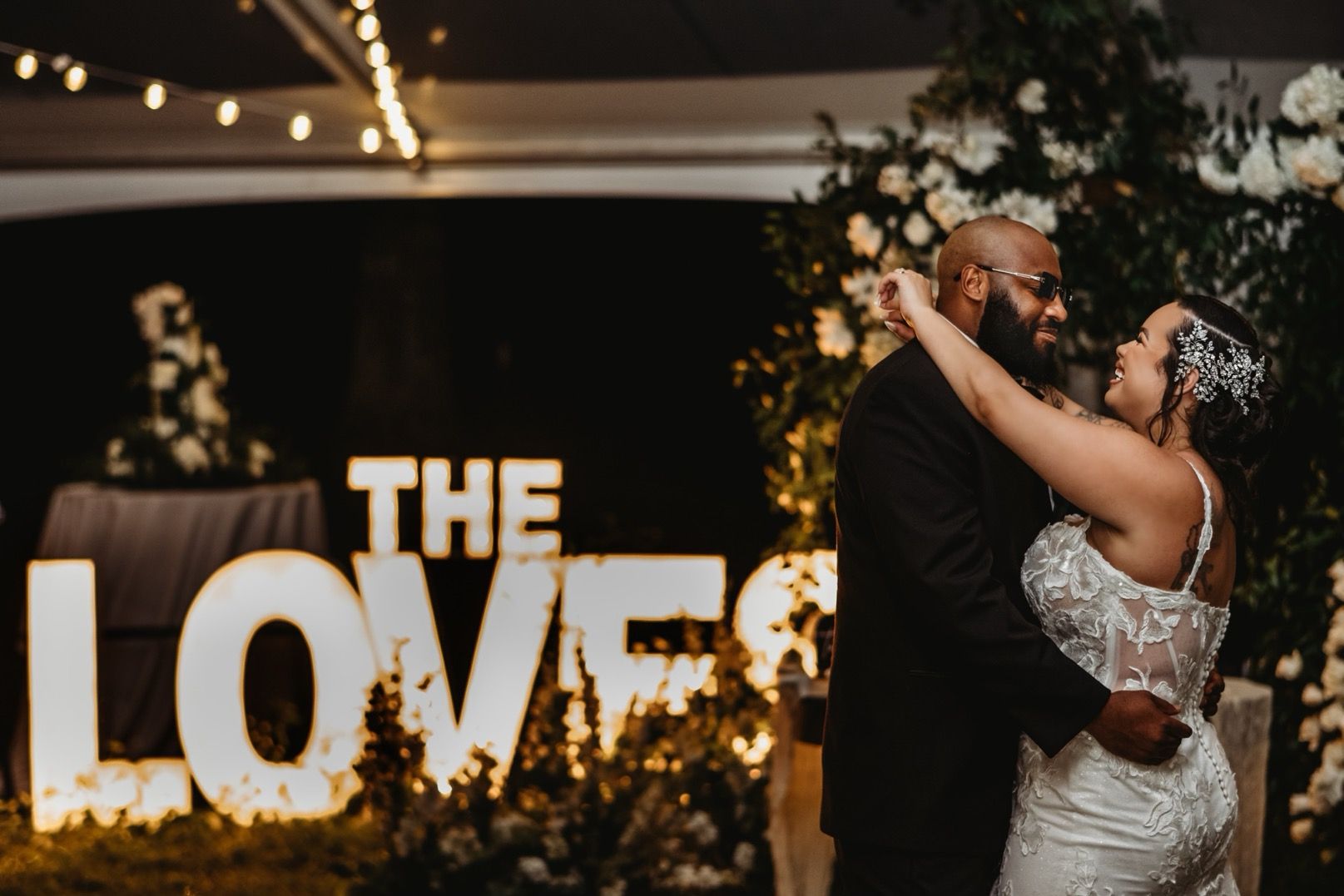 A bride and groom are dancing in front of a sign that says `` the love ''.