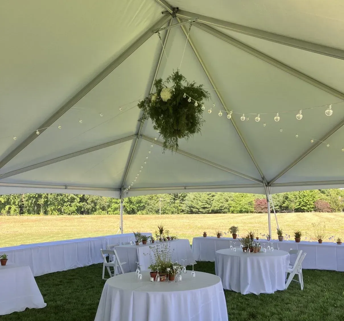 Wedding tent set up with tables, chairs, floral decorations, and string lights.