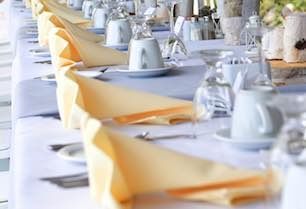 A long table with plates , cups , napkins and glasses on it.