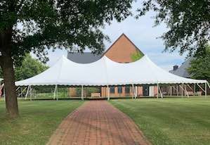A large white tent is sitting on top of a lush green field next to a brick walkway.