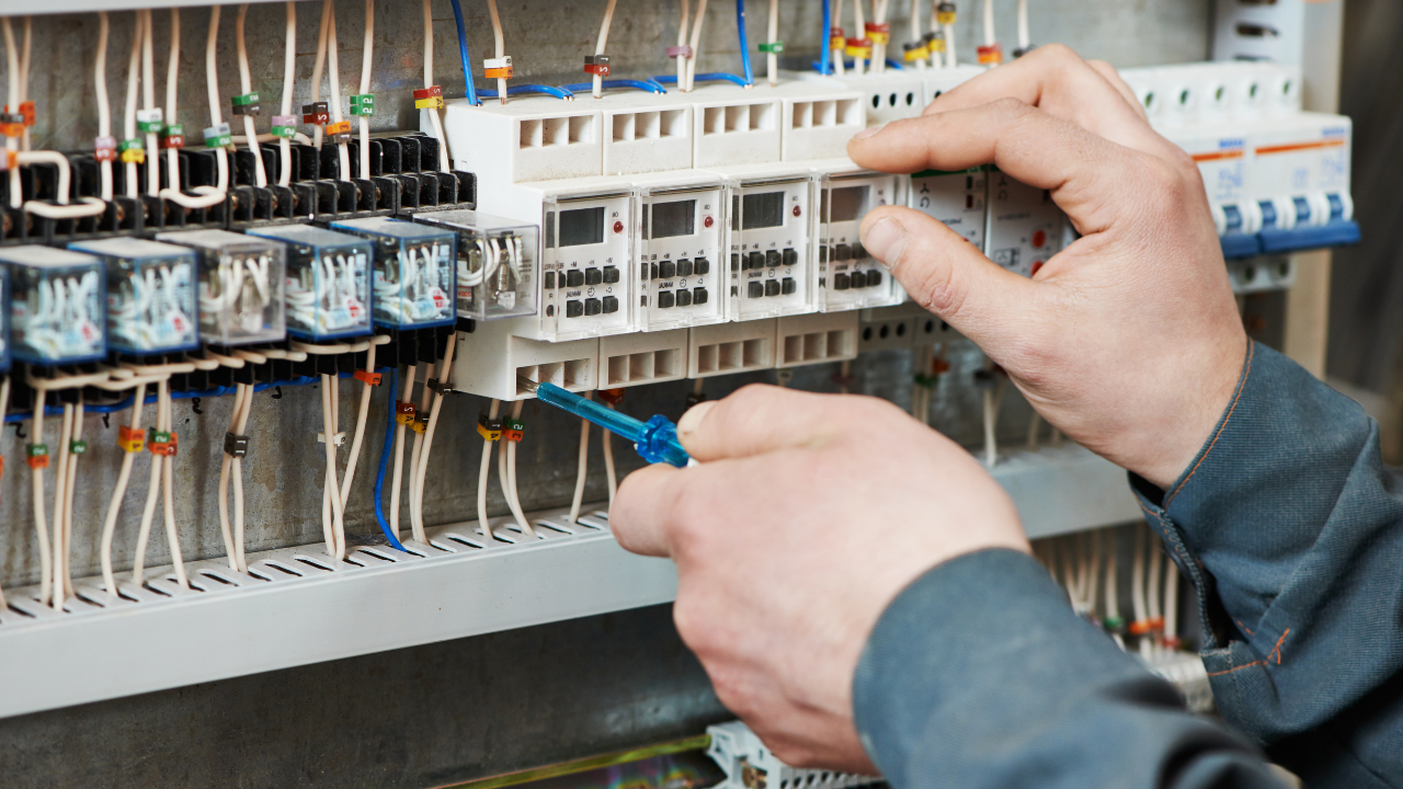 Electrician using a screwdriver to work on a control panel with wires and timers.