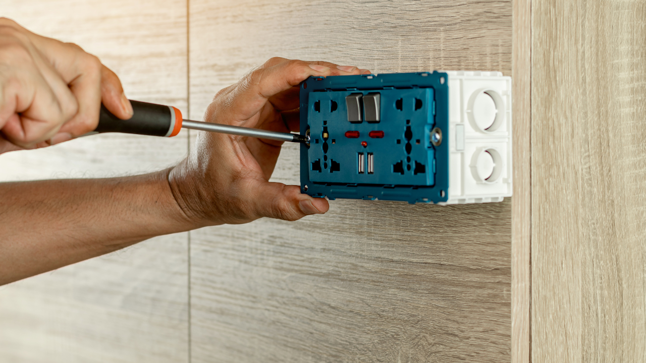 Person using a screwdriver to install an electrical outlet box on a wood-paneled wall.