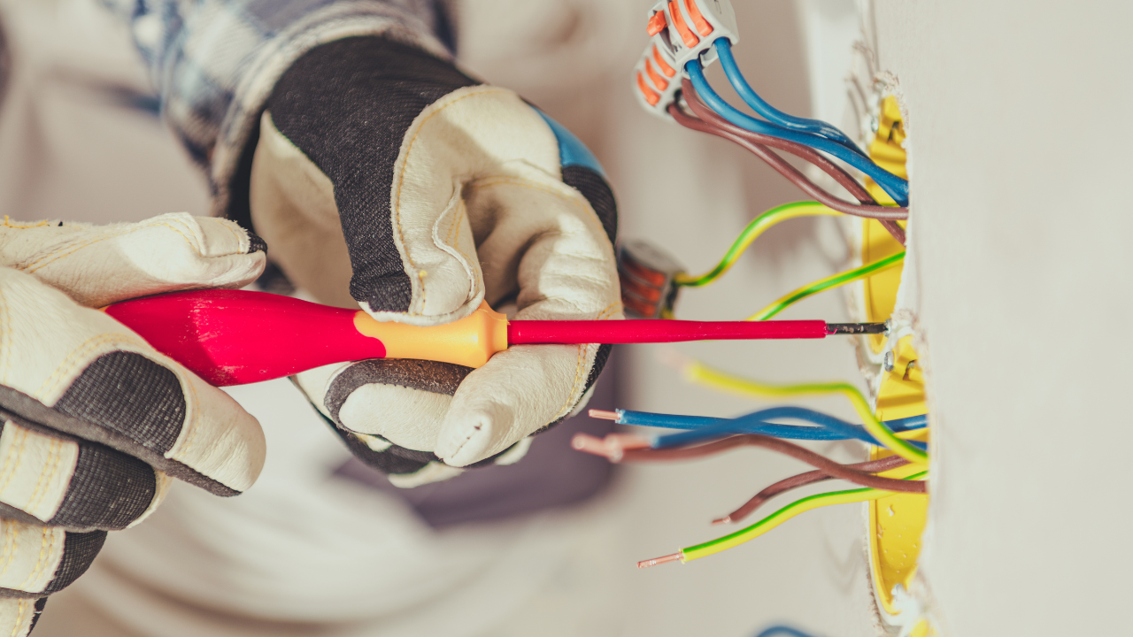 Electrician wiring cables with a screwdriver, wearing gloves.