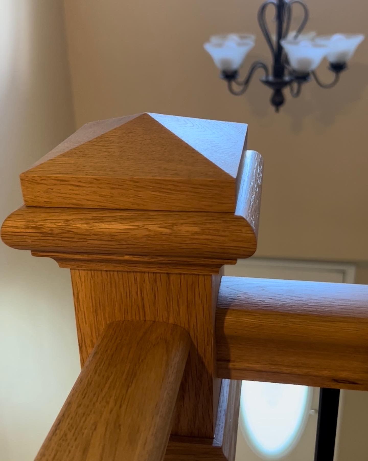 A close up of a wooden railing with a chandelier in the background