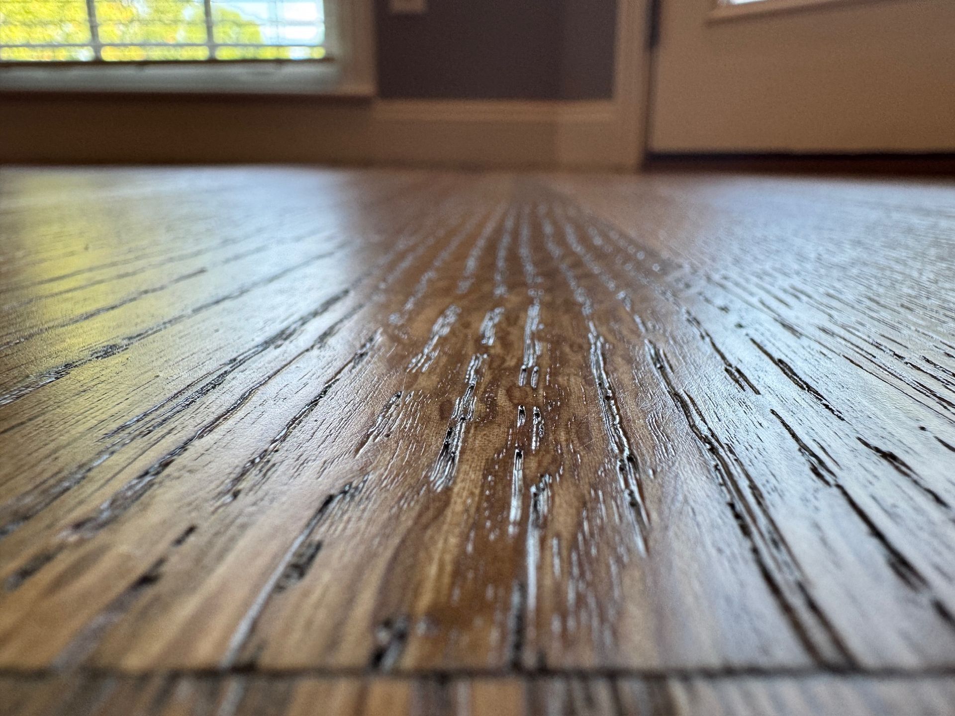 A close up of a wooden floor with a window in the background.