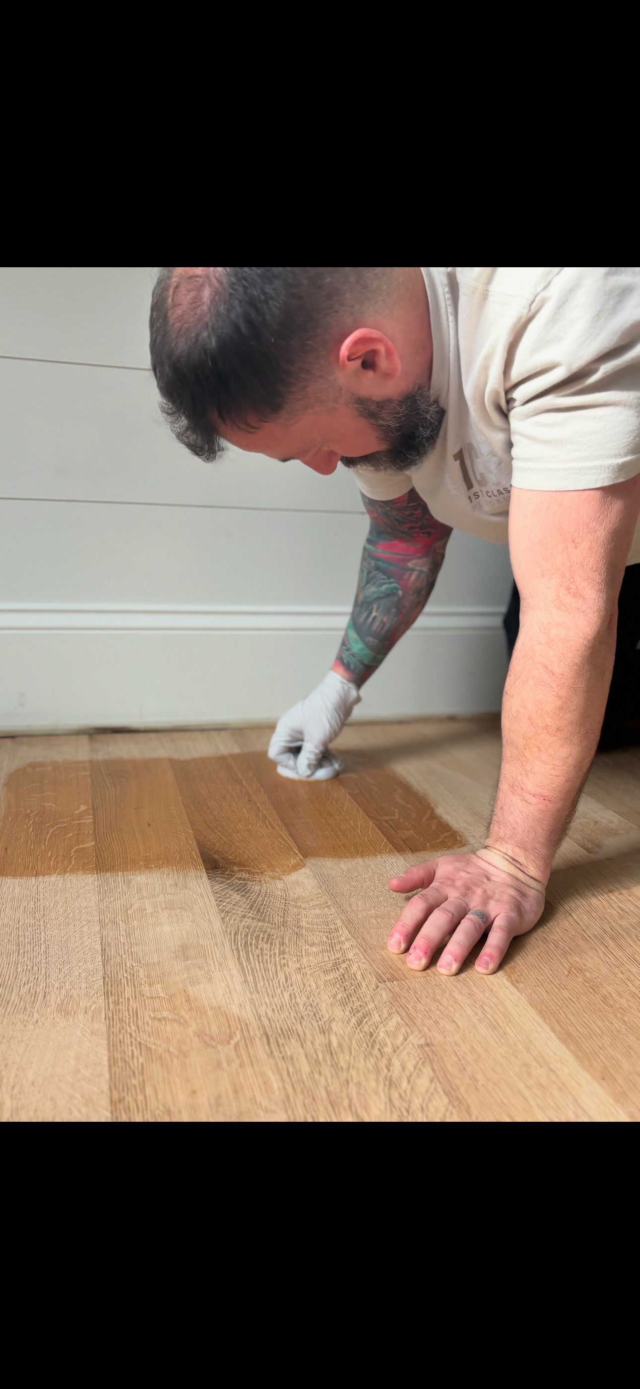 A man is painting a wooden floor with a brush.
