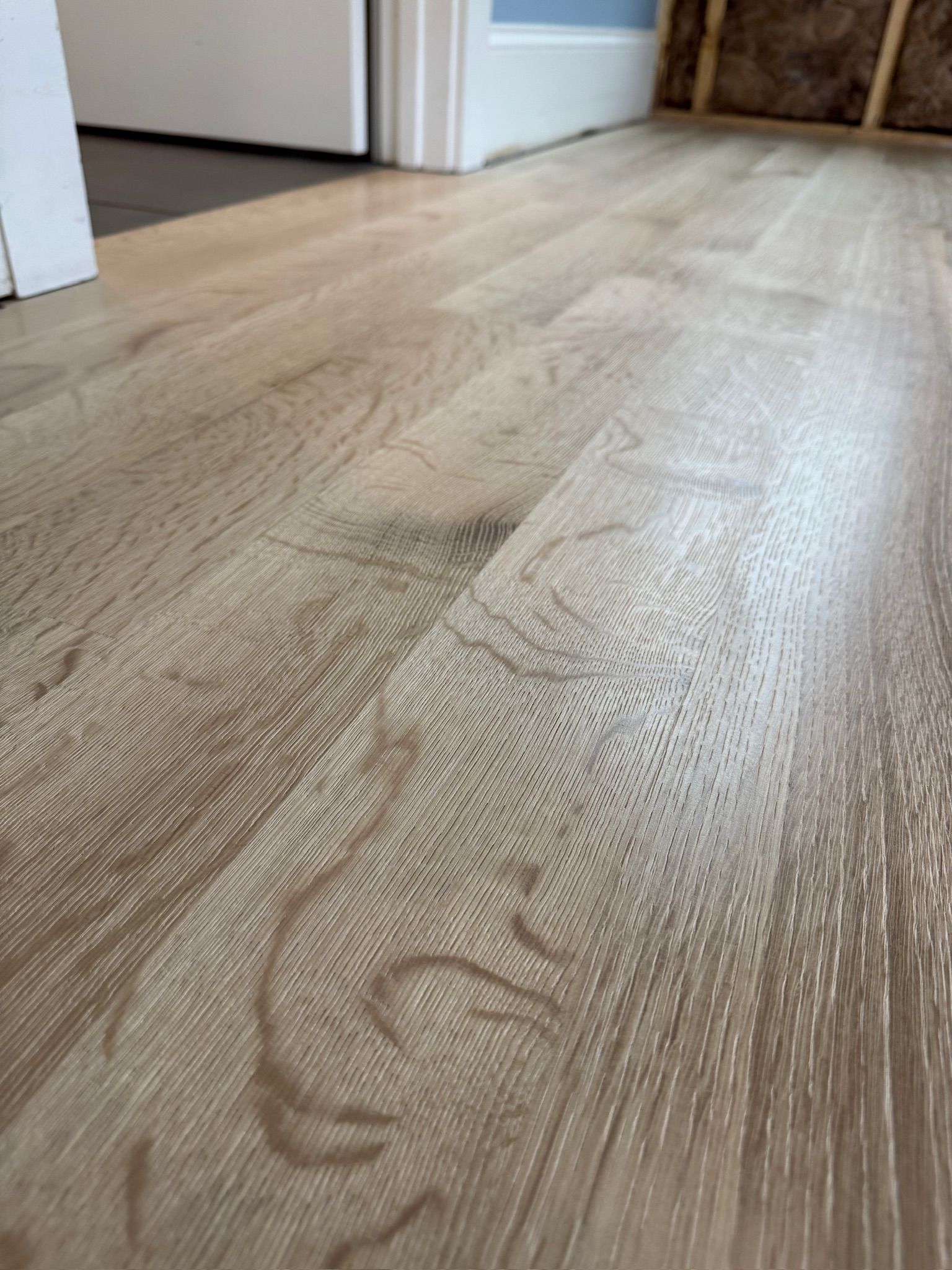 A close up of a wooden floor with a door in the background.