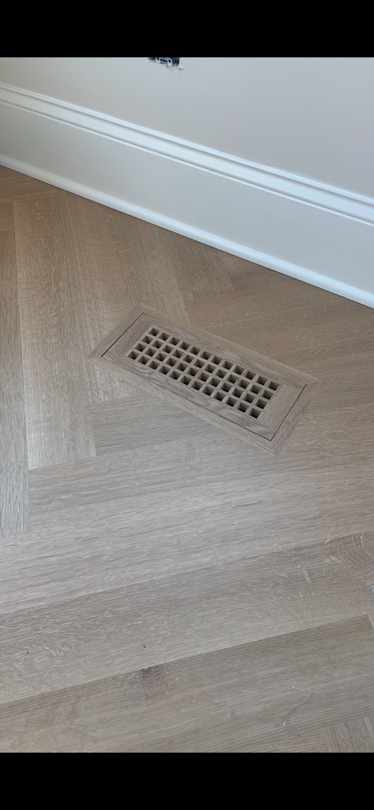 A vent on the floor of a room next to a wall.