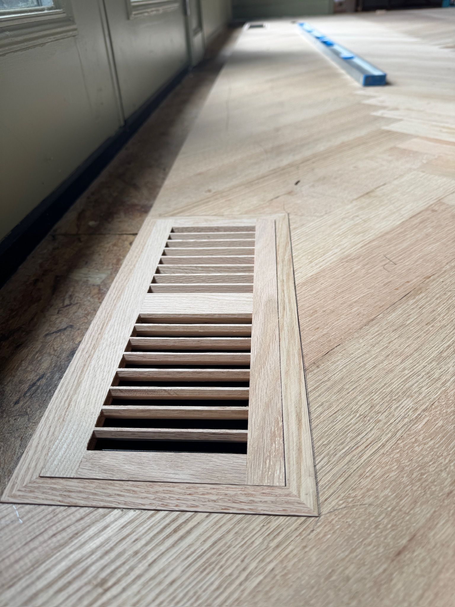 A wooden floor with a ventilation grille on it.