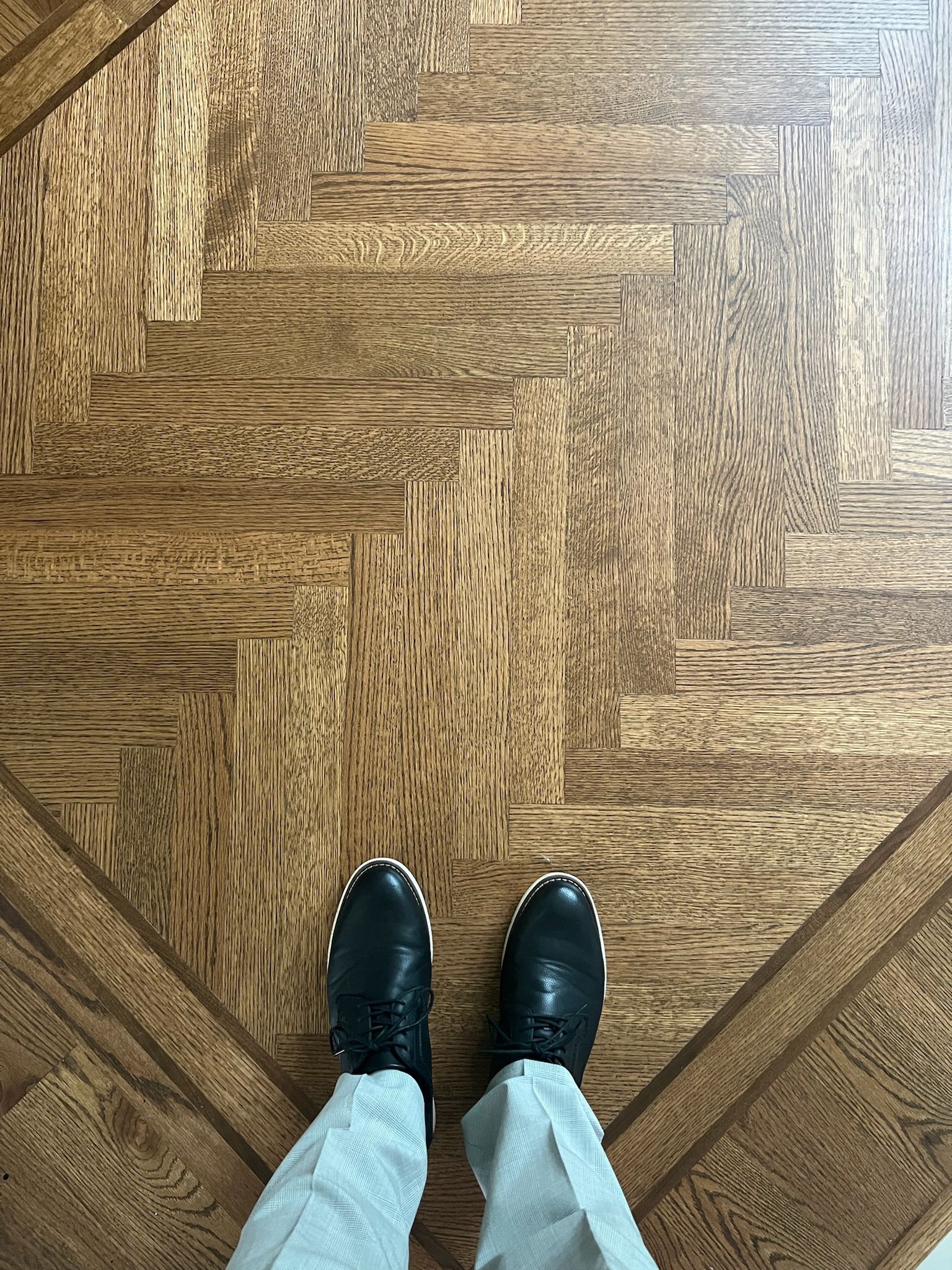 A person is standing on a wooden floor wearing black shoes.
